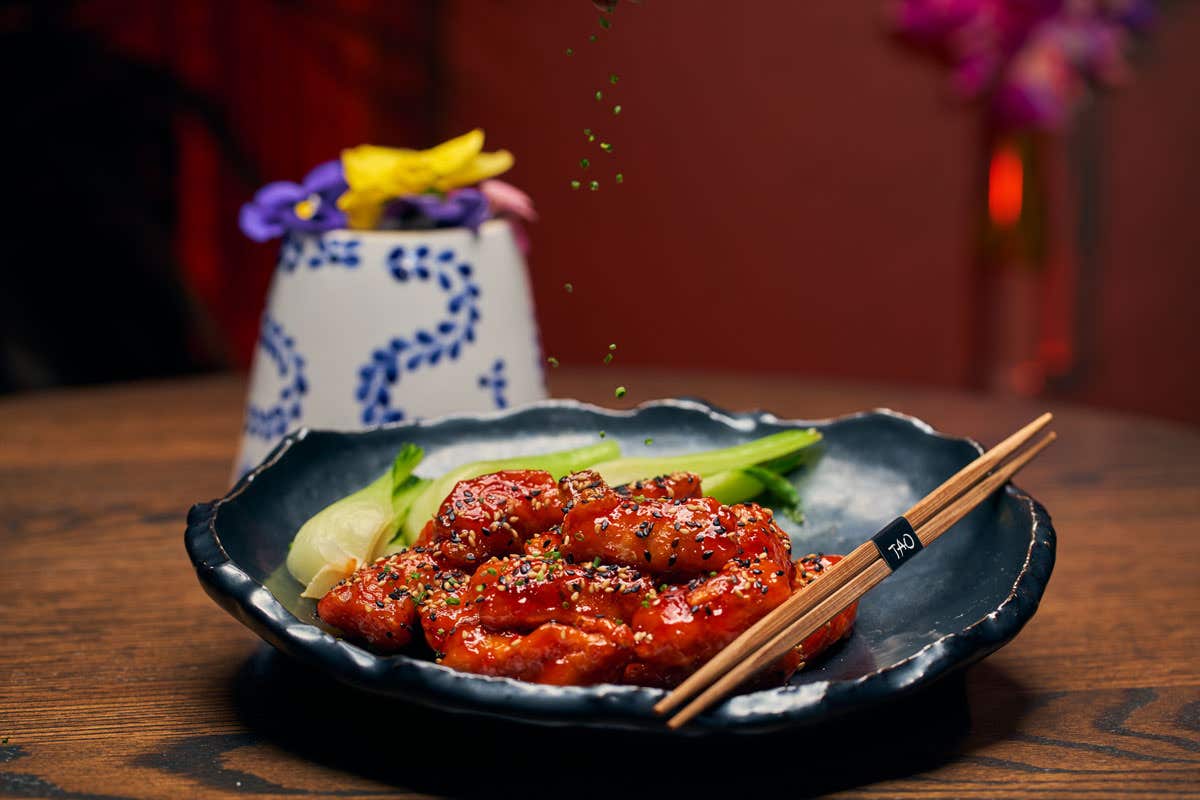 Crispy orange chicken on black plate with vegetables on the side and brown chopsticks on the plate.