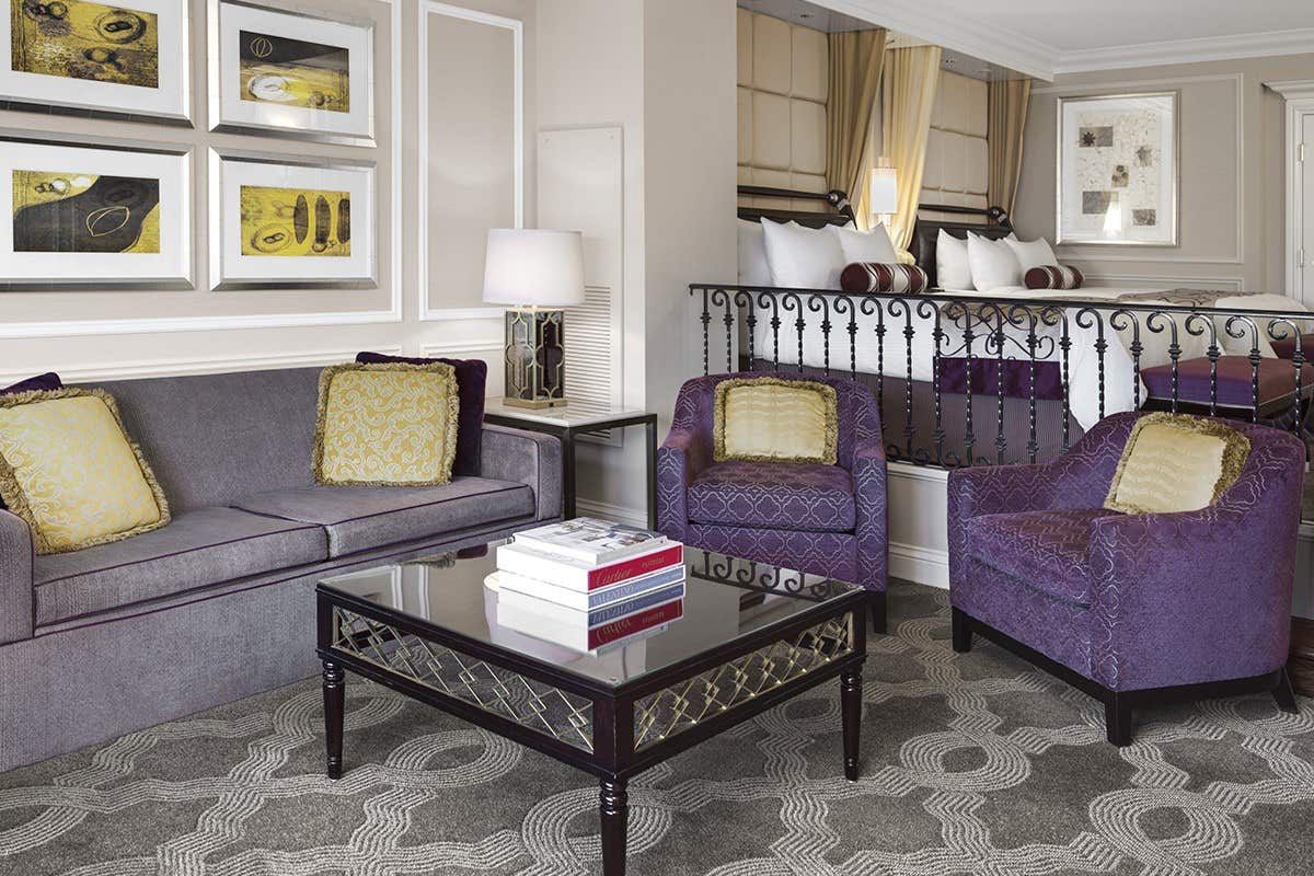 Elegant living area with two purple armchairs, a purple sofa, a glass coffee table, and framed artwork on the walls.