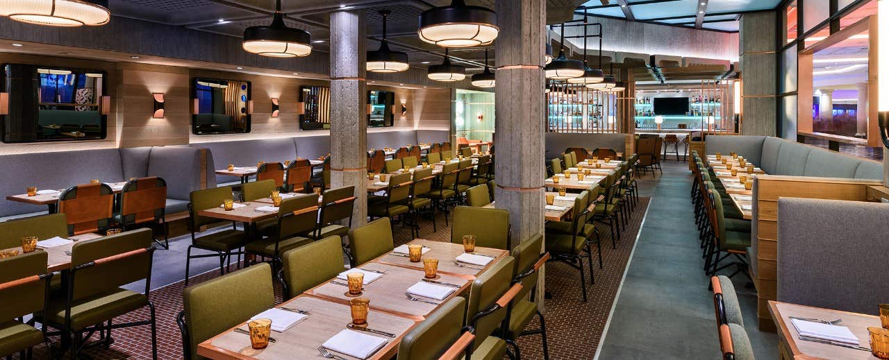 A spacious, modern restaurant with neatly arranged tables, green chairs, and warm lighting creating a cozy ambiance.